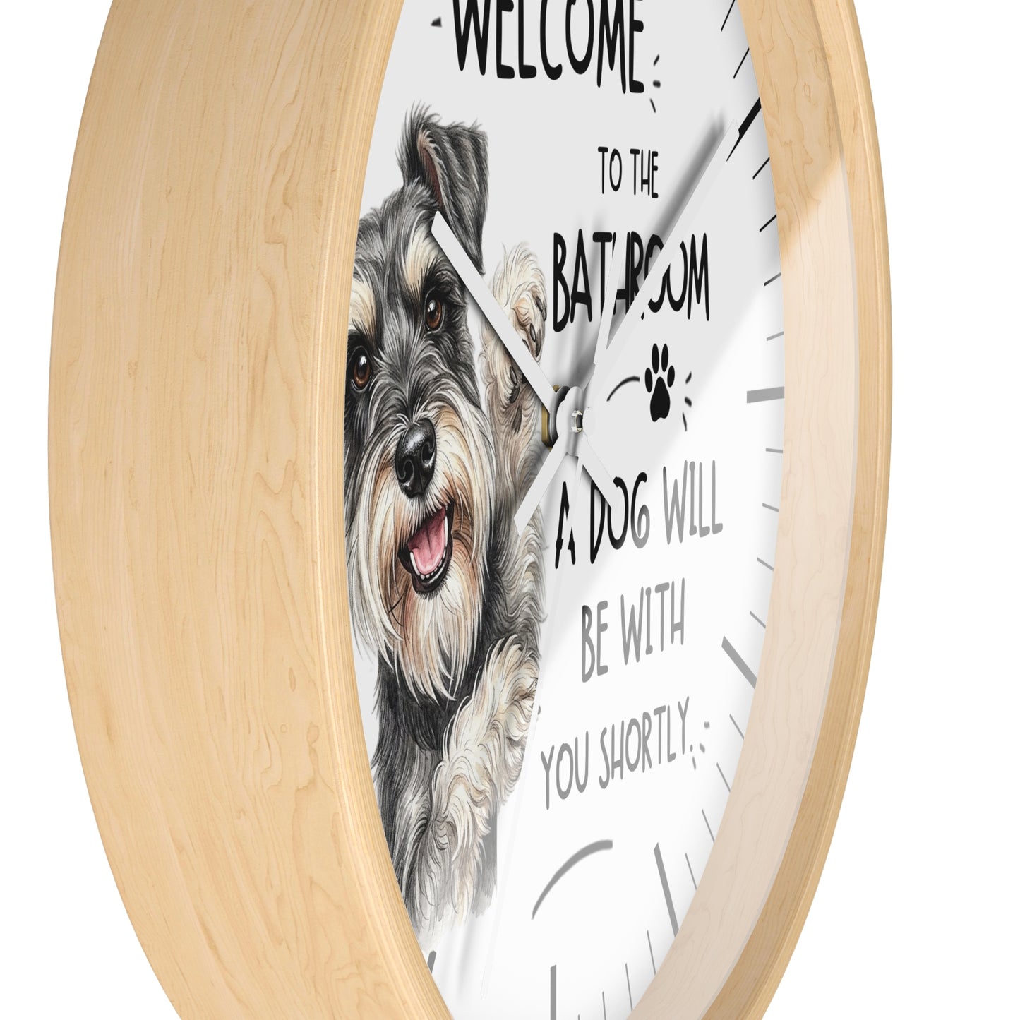 A round wall clock with a light natural wood frame and a white face. The clock face features a detailed illustration of a grey and white dog on the left, alongside the humorous text 'WELCOME TO THE BATROOM A DOG WILL BE WITH YOU SHORTLY' and a small paw print.