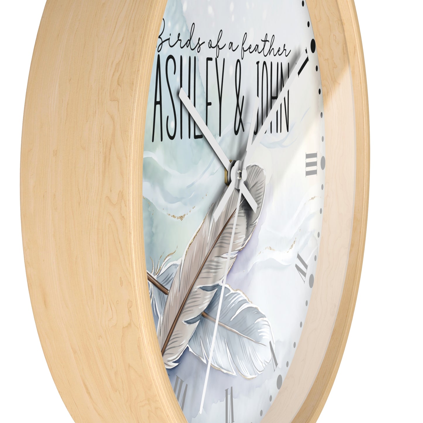 Oval wall clock with a light natural wood frame and a white face featuring a large feather illustration, black script text reading 'birds of a feather', and the names 'ASHLEY & JOHN'.
