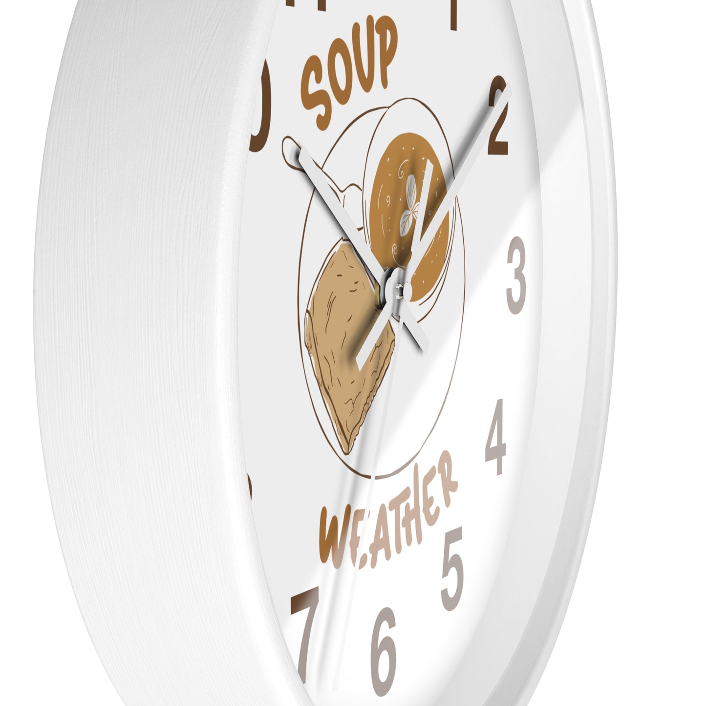 A white round wall clock with a whimsical 'Soup Weather' design. The clock face features brown text reading 'SOUP' at the top and 'WEATHER' at the bottom, with a central illustration of a bowl containing a slice of toast and a spoonful of soup.