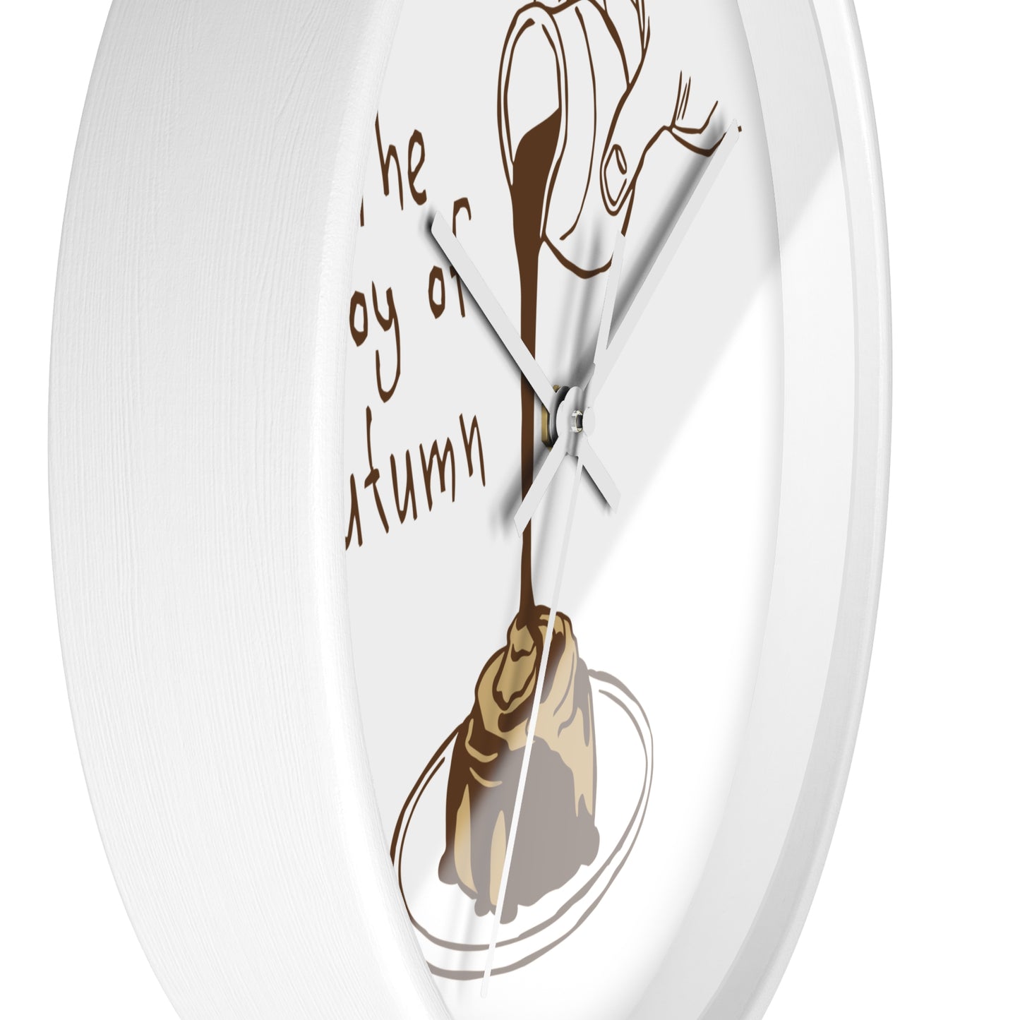 A white round wall clock with a minimalist autumn-themed design. The clock face features a brown illustration of a hand holding a teacup pouring tea into a rolling pastry on a plate, accompanied by the cursive text 'the joy of autumn' in brown.