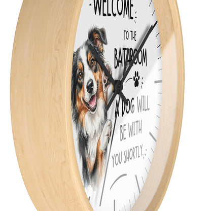 Round wall clock with a light natural wood frame and a white face featuring an illustration of a smiling dog and the text 'WELCOME TO THE BATROOM A DOG WILL BE WITH YOU SHORTLY'.