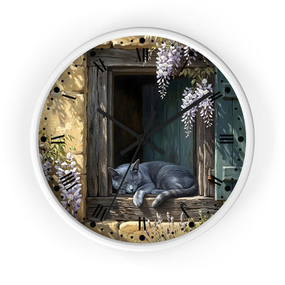 A round wall clock with a white frame and a printed illustration of a gray cat sleeping on a rustic wooden windowsill, surrounded by wisteria flowers and Roman numerals.