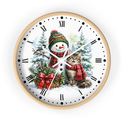 A round wall clock with a light wood frame and a white face featuring a winter holiday illustration of a snowman and a cat in red scarves, surrounded by snowy trees and a basket of greenery.