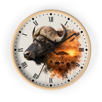 A round wall clock with a light wood frame and a printed design featuring a watercolor-style buffalo head merging into an African savanna sunset scene with silhouettes of animals and trees. The clock face is off-white with black Roman numerals and hour markers.