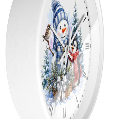 A white round wall clock with a winter-themed illustration on the face, featuring a snowman in a blue striped hat and scarf, a penguin in a red scarf, evergreen trees, and a small bird.