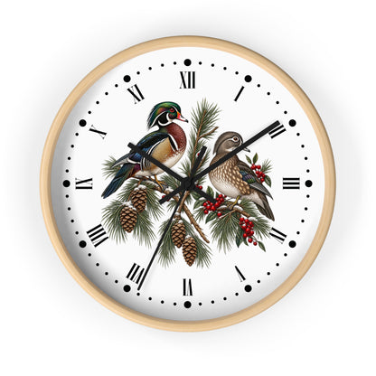 Round wall clock with a light wood frame and a white face featuring two detailed wood ducks perched on pine branches with pinecones and red berries, set against a plain white background.