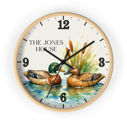 A round wall clock with a light wood frame and a watercolor-style duck scene on the face. The dial shows black Arabic numerals, black clock hands, and the text 'THE JONES HOUSE' near the 12.