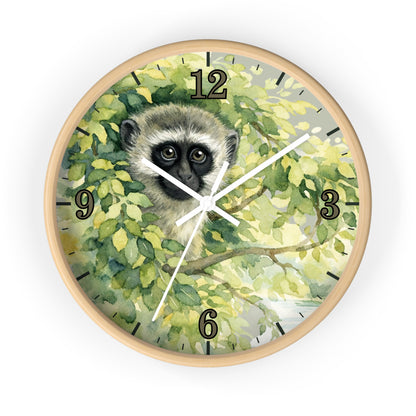 Round wall clock with a light wood frame and a printed watercolor-style face showing a vervet monkey among green leaves, with black Arabic numerals and white clock hands on a white background.