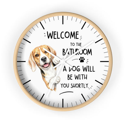A round wall clock with a light wood frame and a white face, featuring a beagle illustration and the text 'WELCOME TO THE BATHROOM A DOG WILL BE WITH YOU SHORTLY.' on a plain white background.