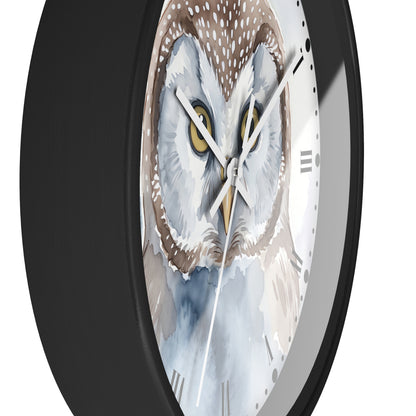A close-up of a round wall clock with a black frame and a watercolor-style owl face on the dial. The owl has white, gray, brown, and blue tones with yellow eyes, and the clock hands are white and gold.