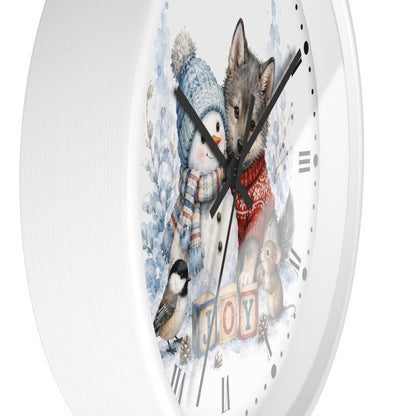 A round white wall clock with a whimsical winter illustration on the face, featuring a penguin, wolf, squirrel, bird, and the word "JOY" in colorful blocks. The clock is shown against a clean white background.