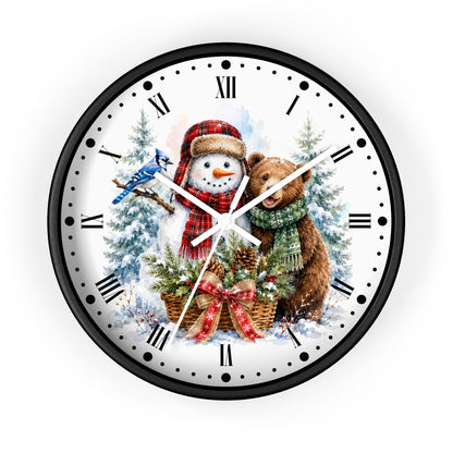 A round wall clock with a black frame and a white face featuring a festive winter illustration of a snowman in a red plaid hat, a brown bear with a green scarf, evergreen trees, and a bluebird, set against a plain white background.