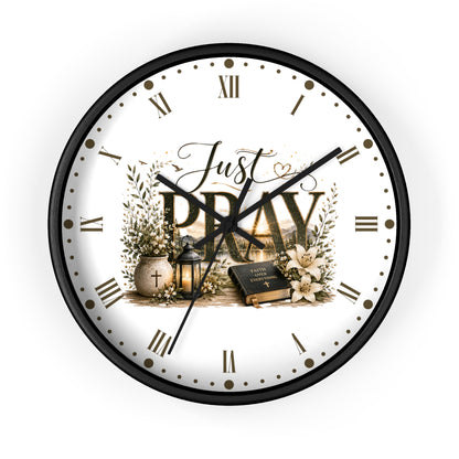 A round wall clock with a black frame and a white face featuring the words 'Just PRAY' in large letters, surrounded by floral and decorative illustrations. The clock is shown against a plain white background.