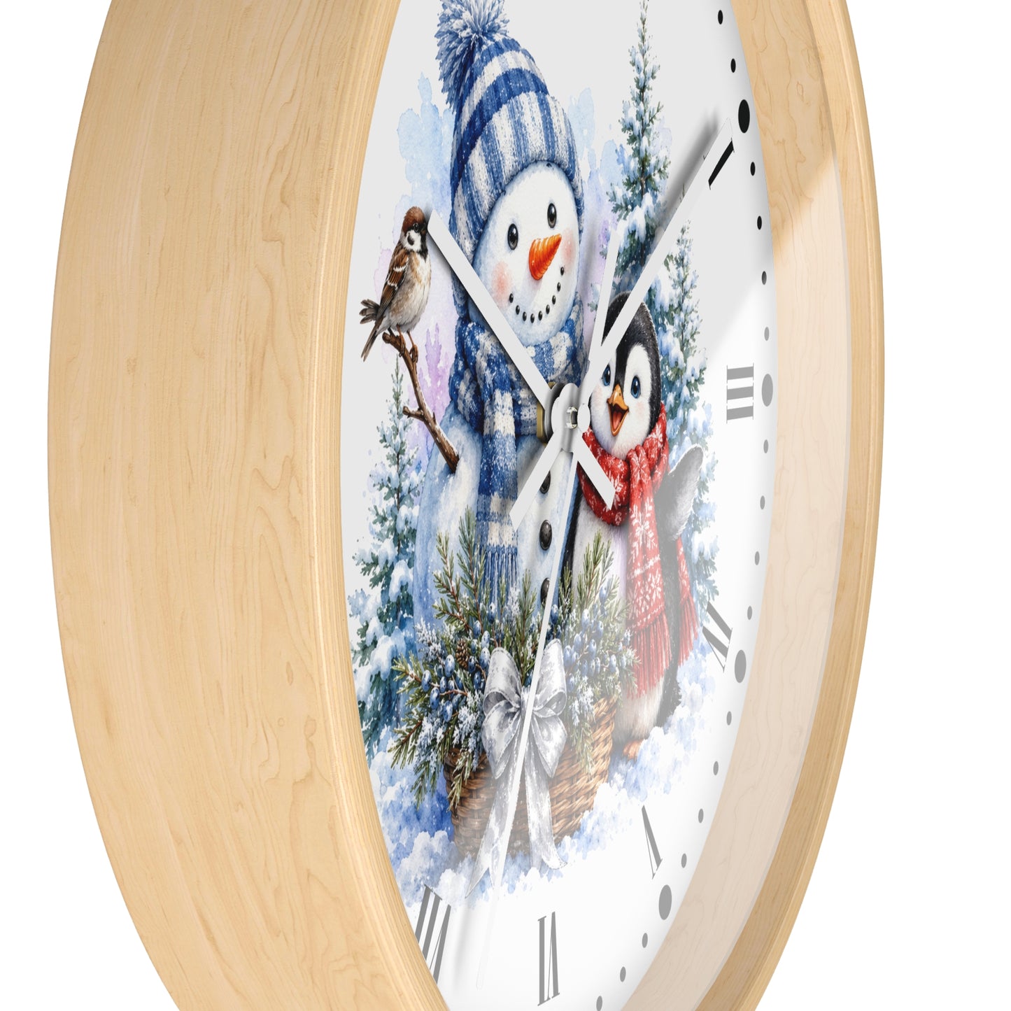 A round wall clock with a light natural wood frame and a white face featuring a winter illustration of a snowman, a penguin, birds, and evergreen trees. The clock is shown at an angle against a plain white background.