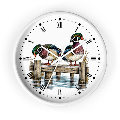 A round white wall clock featuring an illustration of two wood ducks perched on a wooden dock over water, with black Roman numerals and white hands on a clean white background.