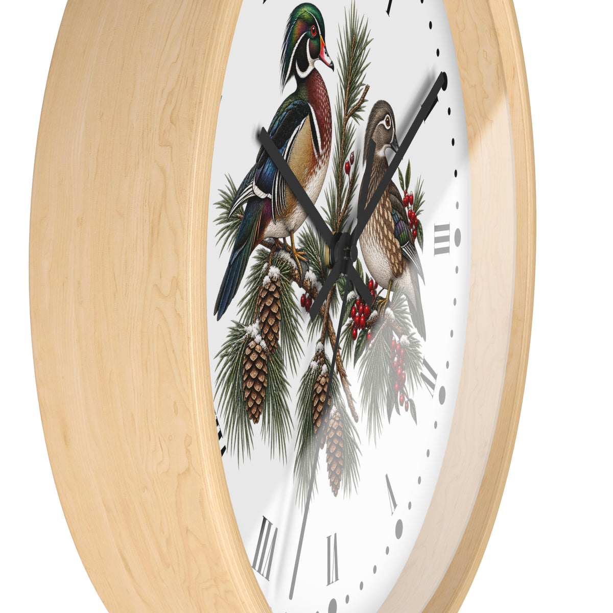 A close-up of a round wall clock with a light natural wood frame and a white face featuring an illustrated woodland scene with two wood ducks, pine branches, pinecones, and red berries.