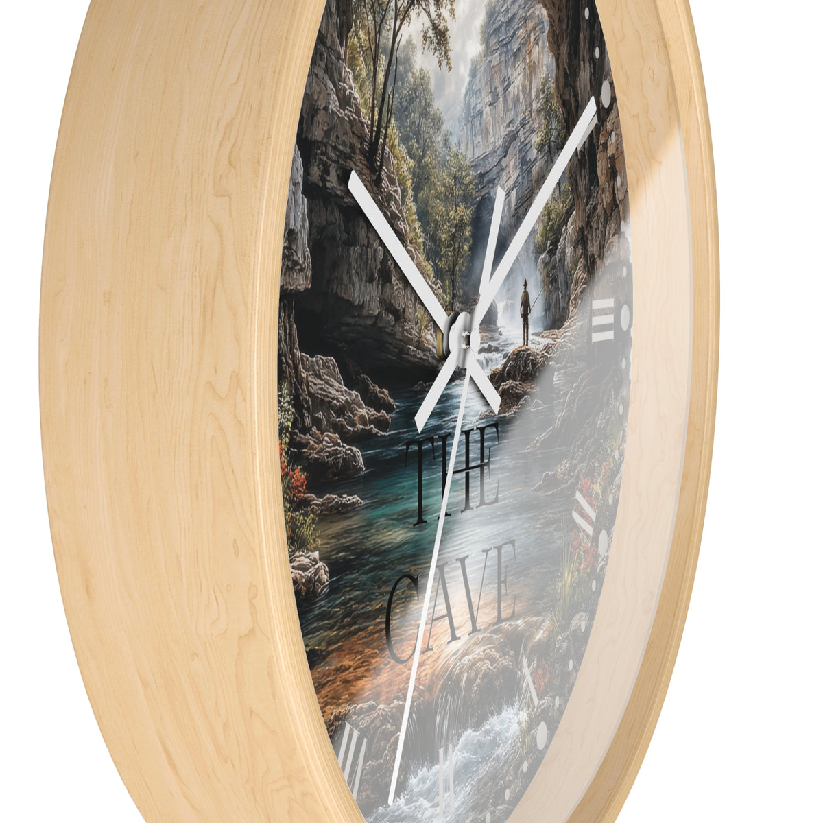 Round wall clock with a light natural wood frame and a printed scenic face showing a cave interior with a river, trees, and the words “THE CAVE.” White clock hands are visible against a plain white background.