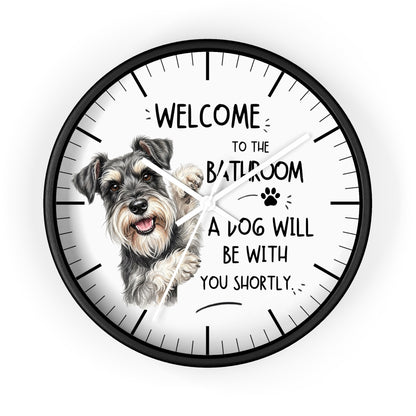 A round wall clock with a black frame and a white face, featuring a hand-drawn Schnauzer dog illustration and the humorous text 'WELCOME TO THE BATHROOM A DOG WILL BE WITH YOU SHORTLY.'.