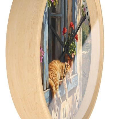 Round wall clock with a light natural wood frame and a printed scenic face showing an orange tabby cat resting by a blue window with red flowers, photographed on a white background.