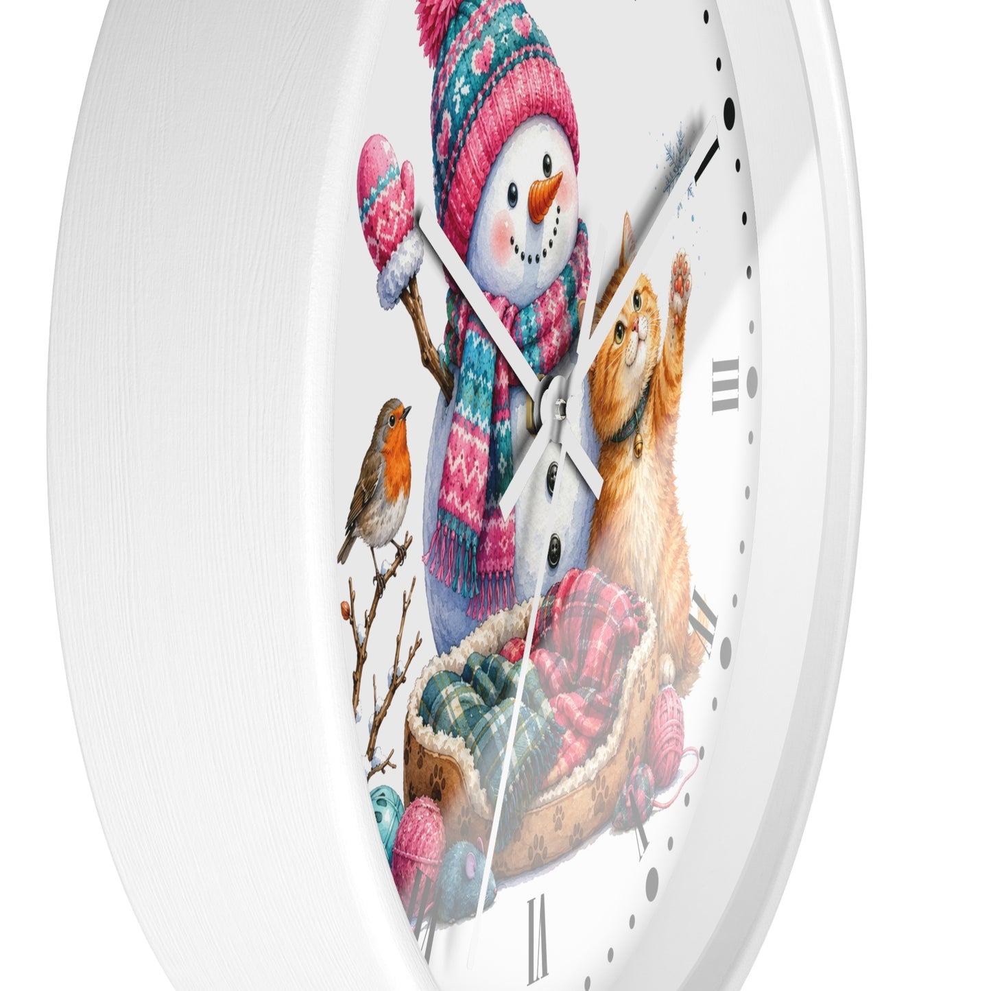 A white round wall clock with a whimsical winter illustration on the face, featuring a snowman in a pink and blue knit hat and scarf, a ginger cat in a basket, a small bird, and winter-themed accents. The clock is shown against a clean white background.