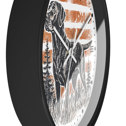 A round wall clock with a black frame and a printed dial featuring a black dog illustration over orange and white horizontal stripes, with black hands and white hour markers.