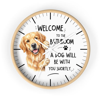 A round wall clock with a light wood frame and a white face, featuring a golden retriever illustration and the text 'WELCOME TO THE BATHROOM A DOG WILL BE WITH YOU SHORTLY.' on a plain white background.