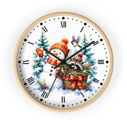 A round wall clock with a light wood frame and a white face featuring a festive winter illustration of a snowman in an orange hat, a raccoon in a basket, evergreen trees, and a bird, with black Roman numerals and hands on a white background.