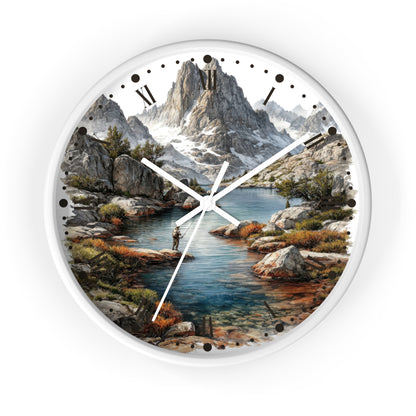 A round wall clock with a white frame and a scenic mountain landscape printed on the face, featuring a river, rocks, trees, and a small figure near the water. The clock is shown against a plain white background.