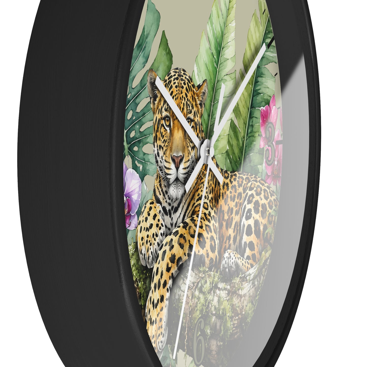 Round wall clock with a black frame and a printed tropical jungle design featuring a leopard, large green leaves, and pink flowers on a light beige background.