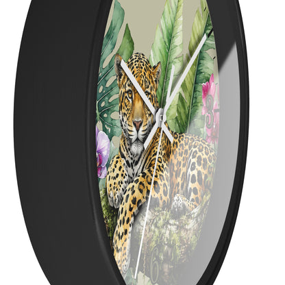 Round wall clock with a black frame and a printed tropical jungle design featuring a leopard, large green leaves, and pink flowers on a light beige background.