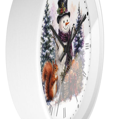 A white round wall clock with a winter illustration on the face, showing a snowman, a squirrel, evergreen trees, and floral elements. The clock has black hands and Roman numeral hour markers on a clean white background.