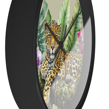 Round wall clock with a black frame and tropical jungle print featuring a leopard, large green leaves, and pink flowers on a light beige background.