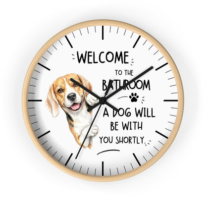 A round wall clock with a light wood frame and a white face, featuring a beagle illustration and the text 'WELCOME TO THE BATHROOM A DOG WILL BE WITH YOU SHORTLY.' on a plain white background.