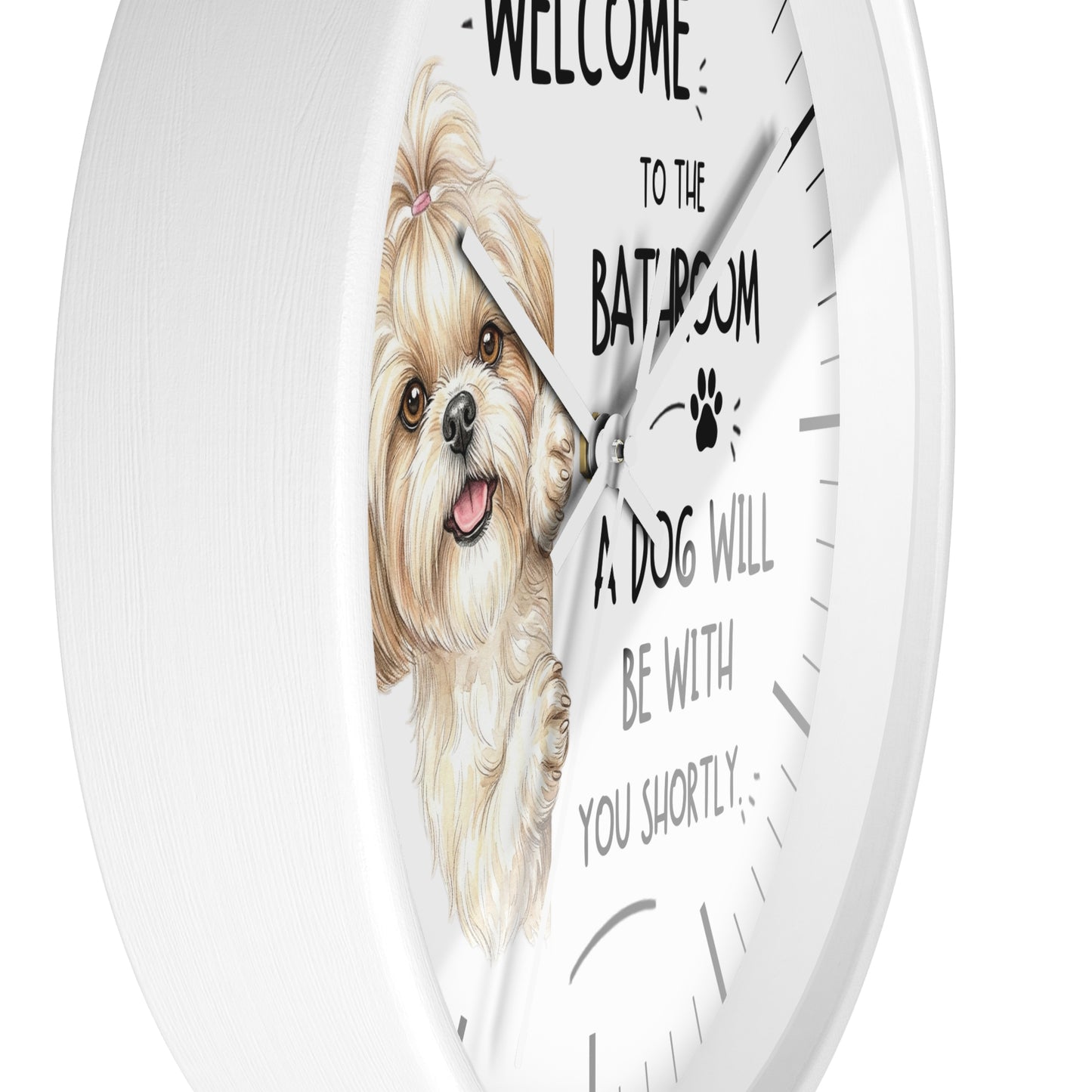 A round white wall clock with a printed face featuring a small fluffy dog illustration and the text 'WELCOME TO THE BATHROOM A DOG WILL BE WITH YOU SHORTLY'.