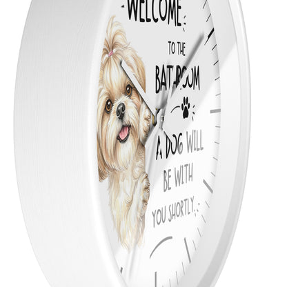 A round white wall clock with a printed face featuring a small fluffy dog illustration and the text 'WELCOME TO THE BATHROOM A DOG WILL BE WITH YOU SHORTLY'.