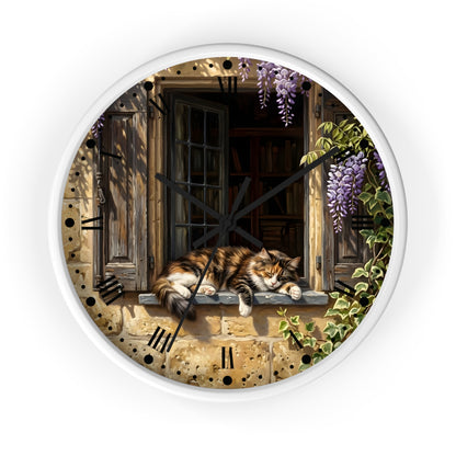 Round wall clock with a white frame and a printed illustration of a fluffy orange-and-white cat resting on a stone windowsill, surrounded by purple wisteria flowers and green ivy. The clock face includes black hands and black Roman numeral hour markers, shown against a plain white background.