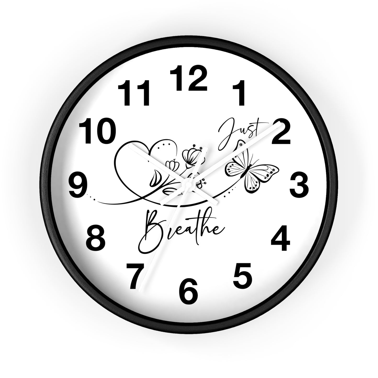 A round wall clock with a black frame and white face, featuring black Arabic numerals and decorative script and line art reading 'Just Breathe' with flowers and a butterfly. The clock is centered on a light gray background.