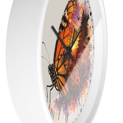 A round white wall clock with a printed butterfly artwork on the face. The design features a large orange and black butterfly over purple and pink abstract paint splatters on a light background.