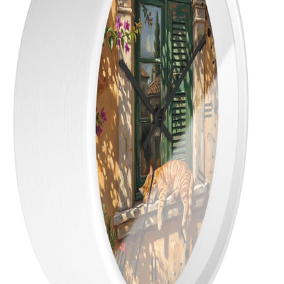 Oval wall clock with a white frame and a printed illustration of a sunlit courtyard scene featuring a green shuttered door, shadow patterns, and an orange tabby cat on a windowsill.