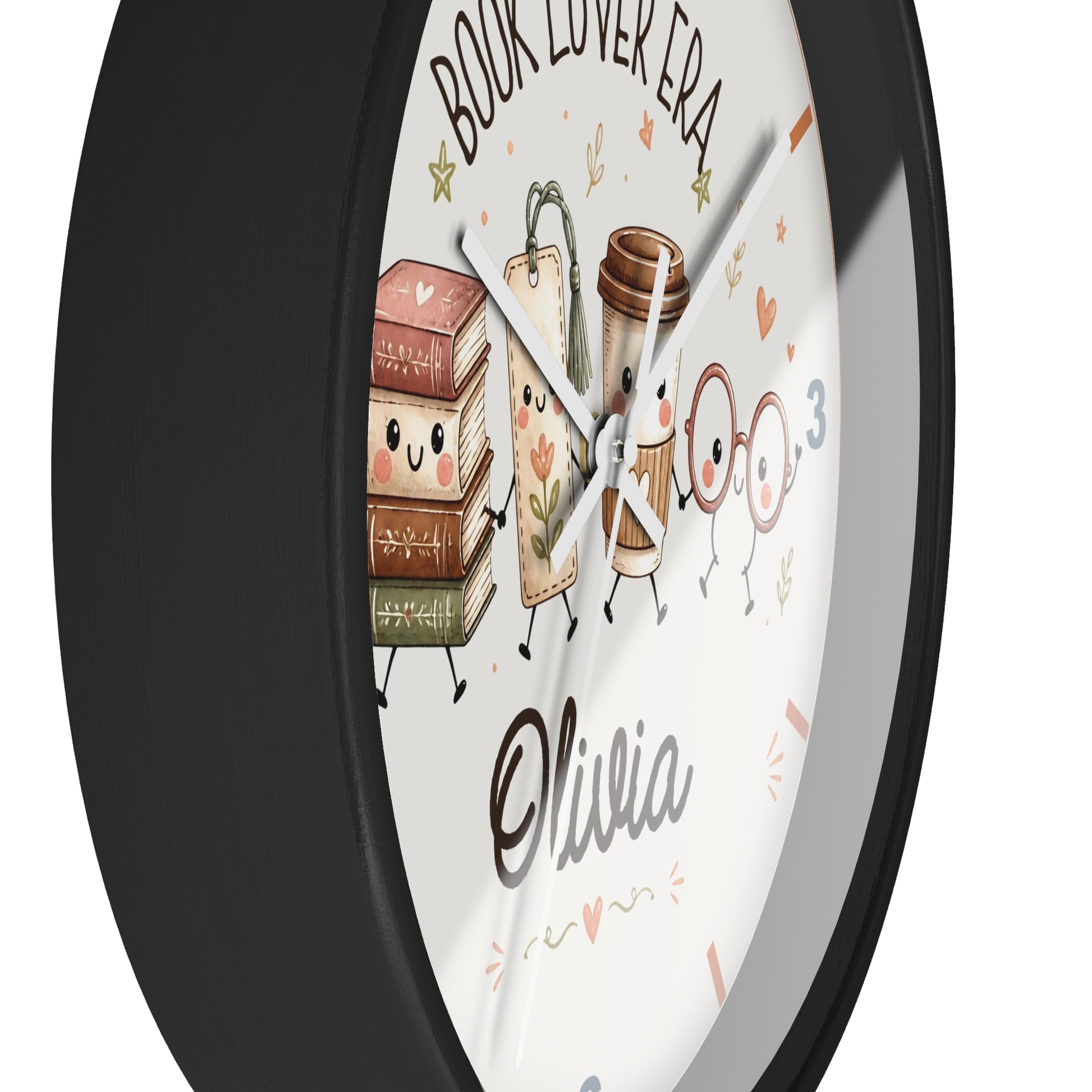 A round wall clock with a black frame and a white face featuring cute illustrated books, a coffee cup, glasses, and the text 'BOOK LOVER ERA' and 'Olivia'.