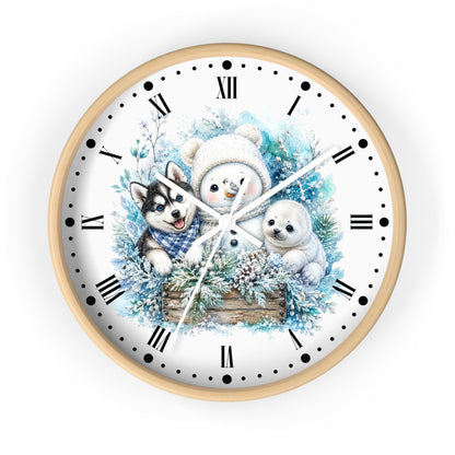 A round wall clock with a light wood frame and a white face, featuring a winter illustration of a snowman, a husky, a seal, and evergreen branches. The clock uses black Roman numerals and markers with white hands.