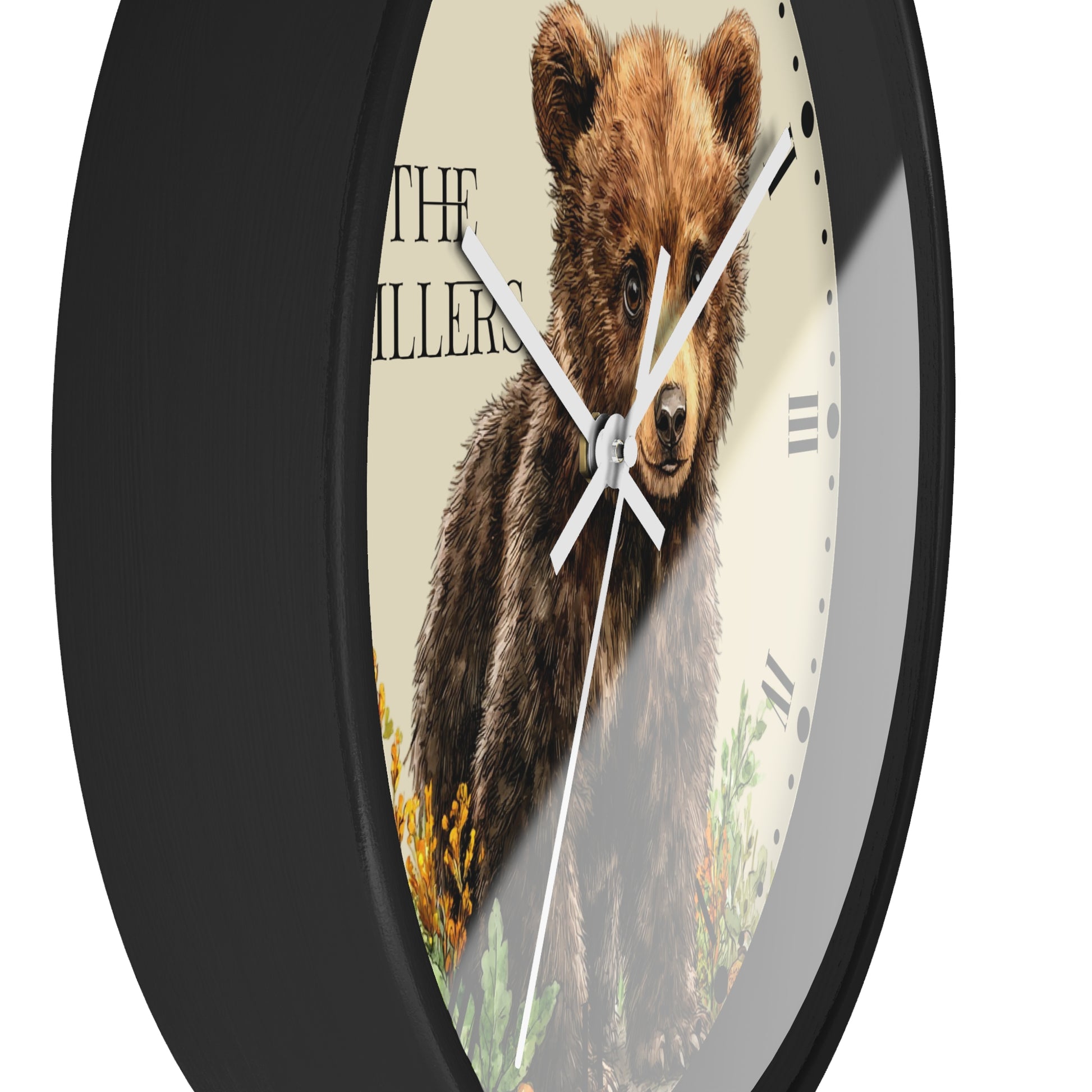 A round wall clock with a black frame and a printed face showing a brown bear illustration over a cream background, with black Roman numerals and white hands.