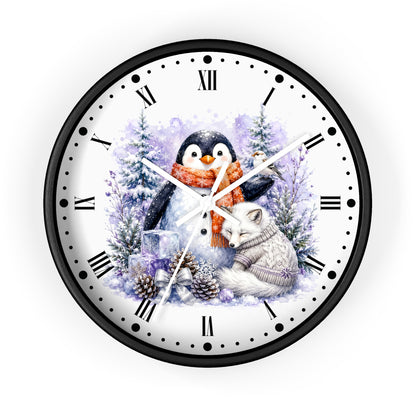 A round wall clock with a black frame and white face, featuring a winter illustration of a penguin in an orange scarf and a white fox in a sweater, surrounded by snowy trees and pinecones. The clock uses black Roman numerals and black minute markers.