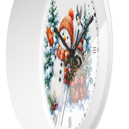 A white round wall clock with a festive winter illustration on the face, featuring a snowman in an orange knit hat and scarf, evergreen trees, a bird, and a raccoon near a red bow and wreath.