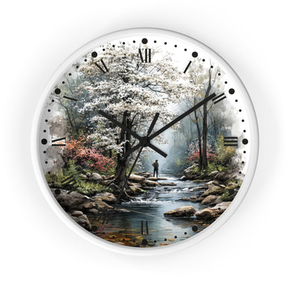Round wall clock with a white frame and a scenic landscape print featuring a stream, trees, rocks, and a small figure, with black Roman numerals and hands on a white background.