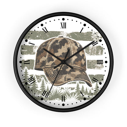 A round wall clock with a black frame and Roman numerals, featuring a camouflage baseball cap and a forest landscape design on a white background.
