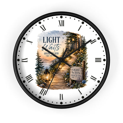 A round wall clock with a black frame and a white face featuring a scenic forest path illustration and the text 'LIGHT Waits AROUND THE Bend' .' Roman numerals mark the hours, with black hands and a small central decorative inset.