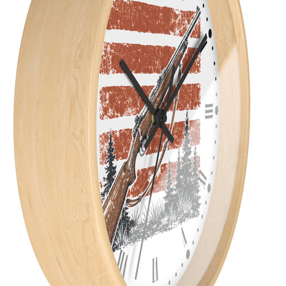 Round wall clock with a light natural wood frame and a white face featuring a rustic red-and-white striped background, a brown rifle illustration, black tree silhouettes, and black Roman numerals.