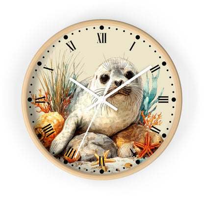 A round wall clock with a light wood frame and a detailed illustration of a seal sitting among rocks, starfish, seashells, and seaweed. The clock face is cream with black Roman numerals and black dot hour markers, and the hands are white.