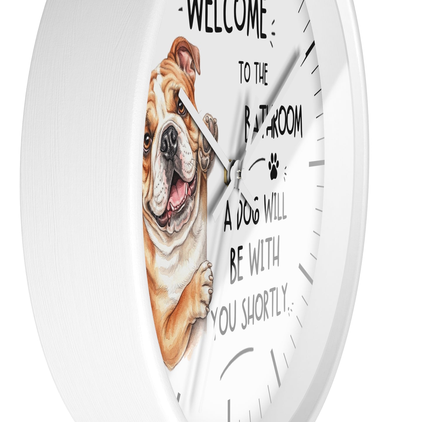 A white round wall clock with a humorous pet message printed on the face: 'WELCOME TO THE BATHROOM A DOG WILL BE WITH YOU SHORTLY.' The clock face features a detailed illustration of a brown and white bulldog peeking in from the left.